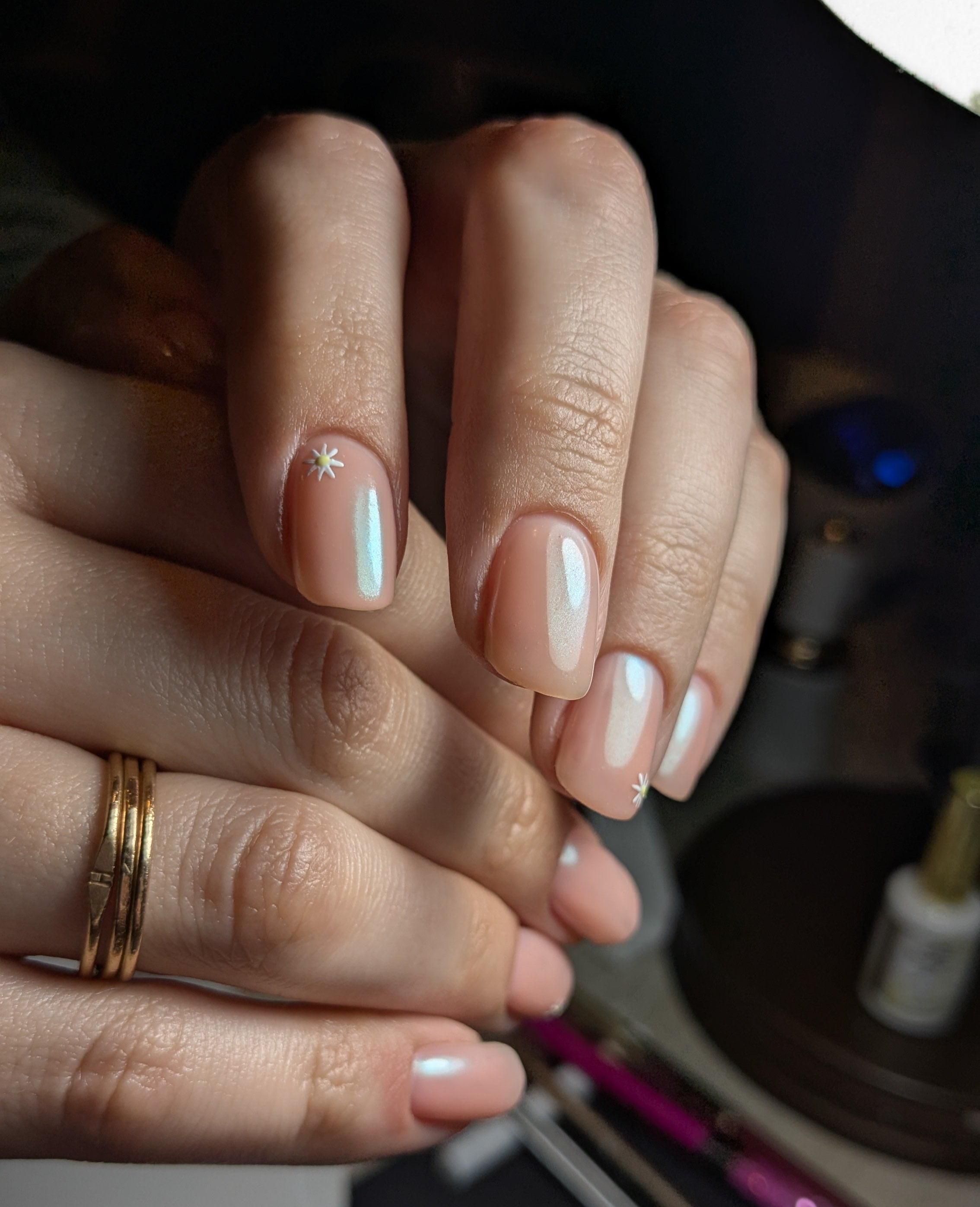Pink gel polish on nails with nail technician workspace in background.